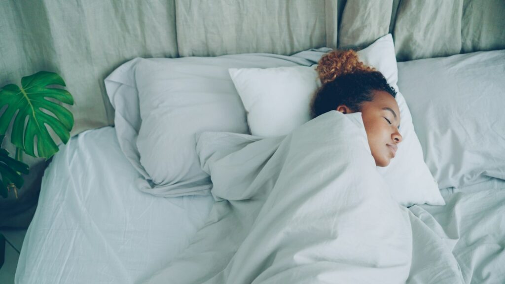 Junge Frau schläft entspannt im hellen Bett – besser schlafen durch Routine