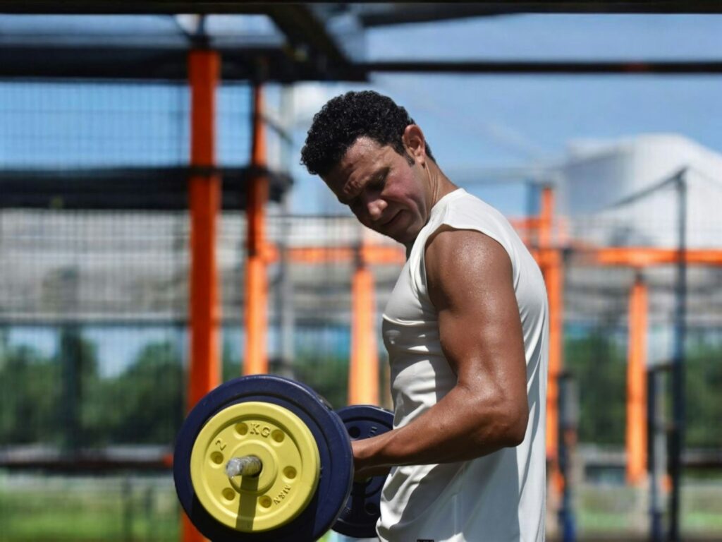 Mann trainiert mit Gewichten im Outdoor-Gym – Bizeps Übungen unter freiem Himmel