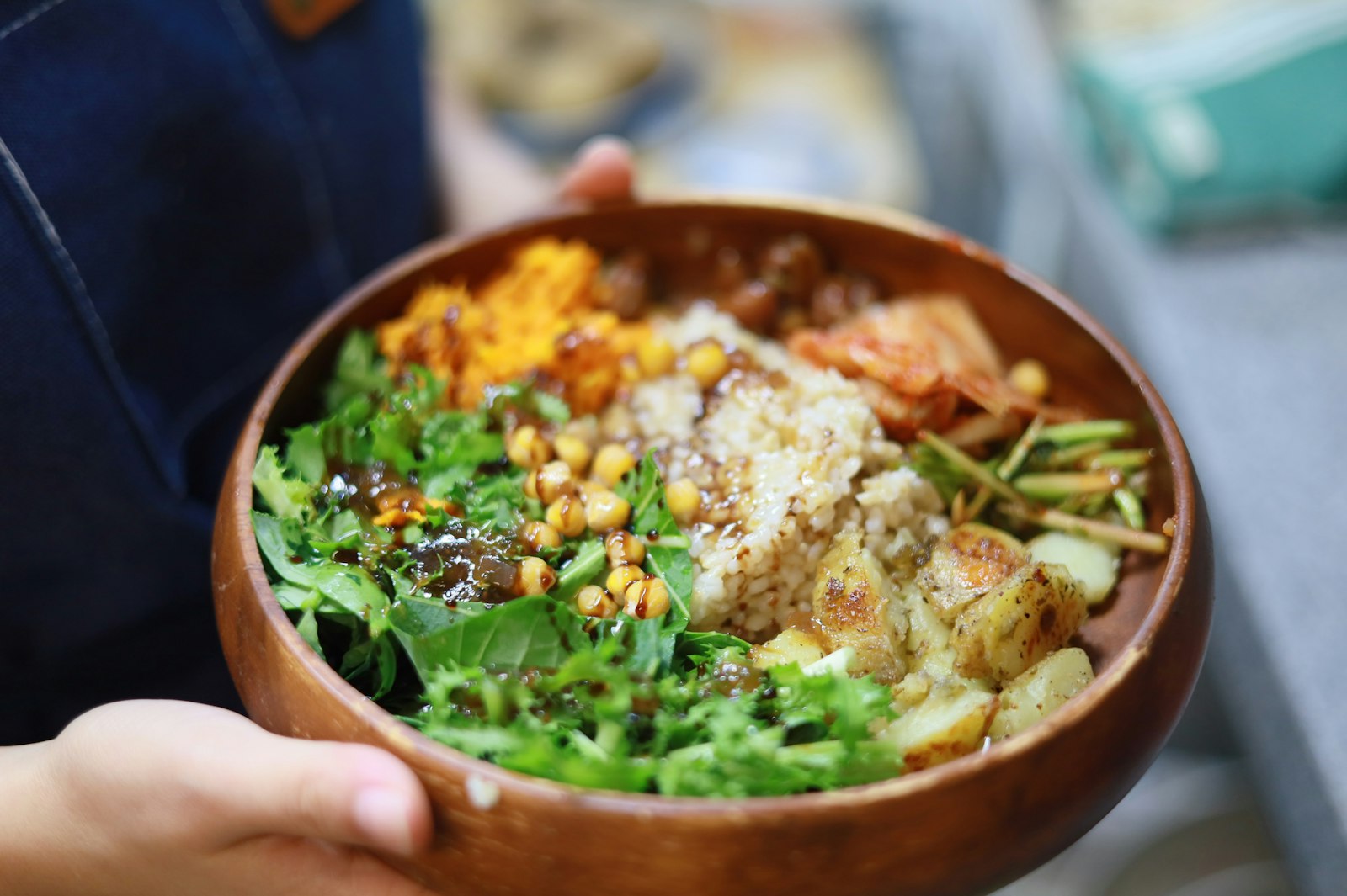 Buddha Bowl: Holzschale mit Reis, Kichererbsen, grünem Blattgemüse und Kartoffeln als Buddha-Bowl