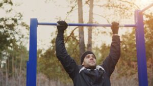 Mann trainiert Klimmzüge an einer Stange im Freien – Calisthenics Übungen draußen