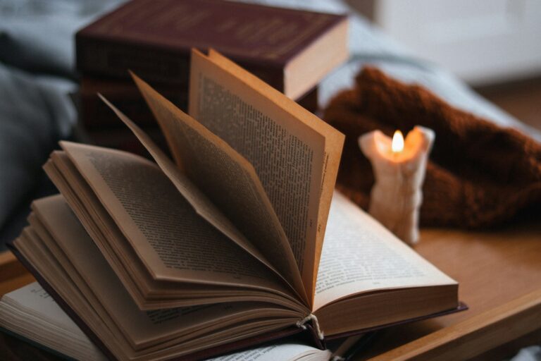Aufgeschlagenes Buch neben einer brennenden Kerze auf einem Tisch am Abend
