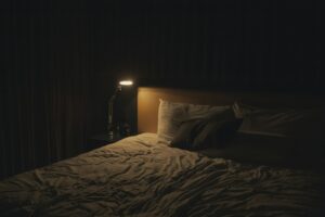Warm leuchtende Nachttischlampe neben einem ruhigen, gemachten Bett am Abend