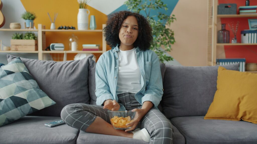 Junge Frau isst abends Chips auf dem Sofa und möchte Heißhunger stoppen