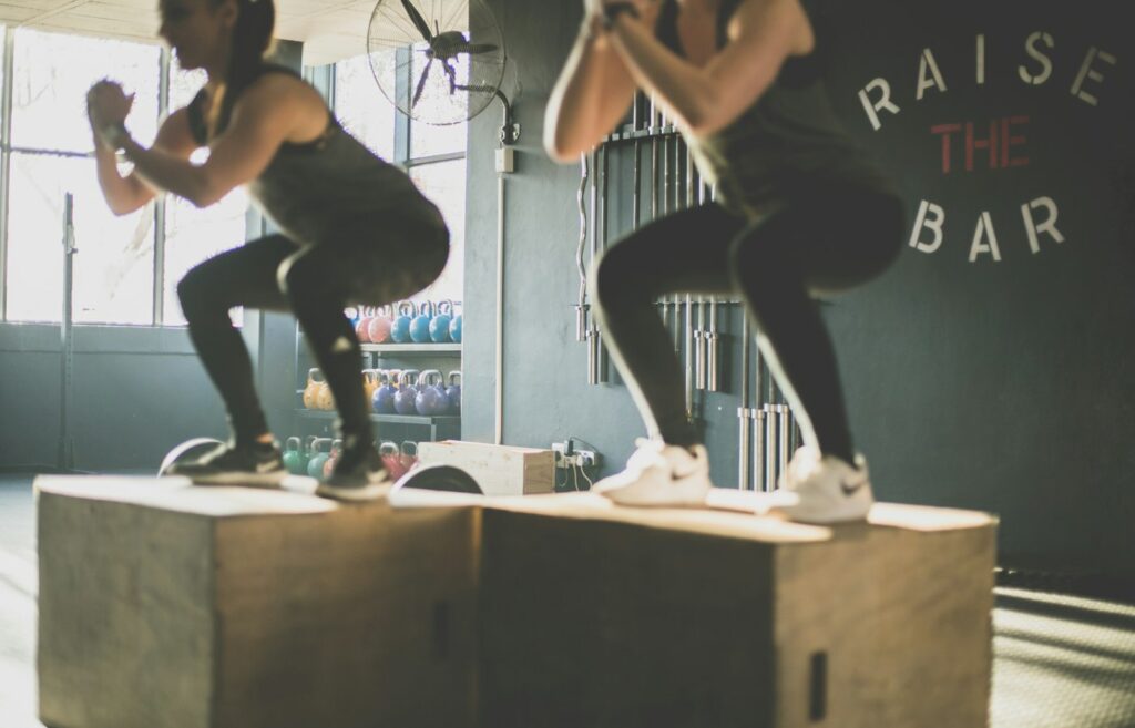 Zwei Personen machen Box Jumps auf Holzkisten beim HIIT Training im Studio