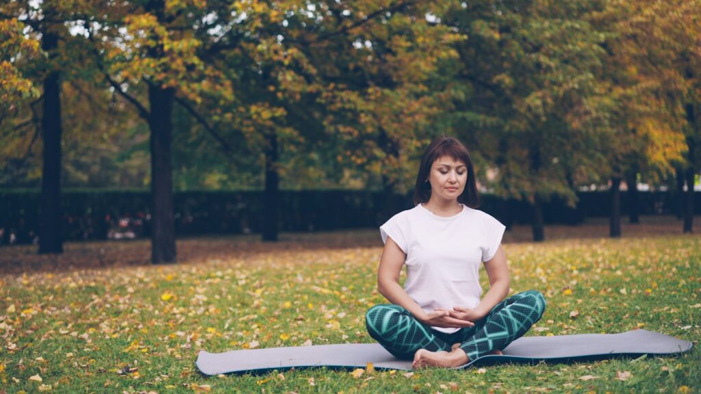 Frau meditiert entspannt auf einer Yogamatte im Park gegen innere Unruhe