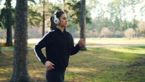 Joggen für Anfänger: Junge Frau joggt mit Kopfhörern entspannt durch einen grünen Park