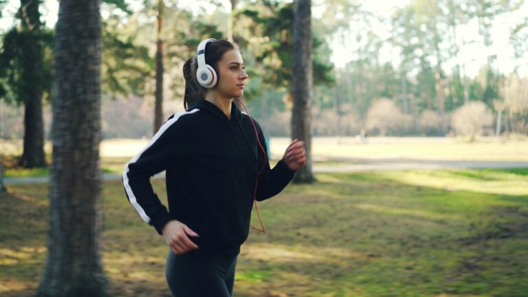 Laufen für Anfänger: Junge Frau joggt mit Kopfhörern entspannt durch einen grünen Park