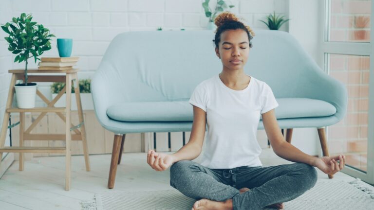 Meditation für Anfänger: Junge Frau meditiert ruhig auf dem Boden in ihrer Wohnung