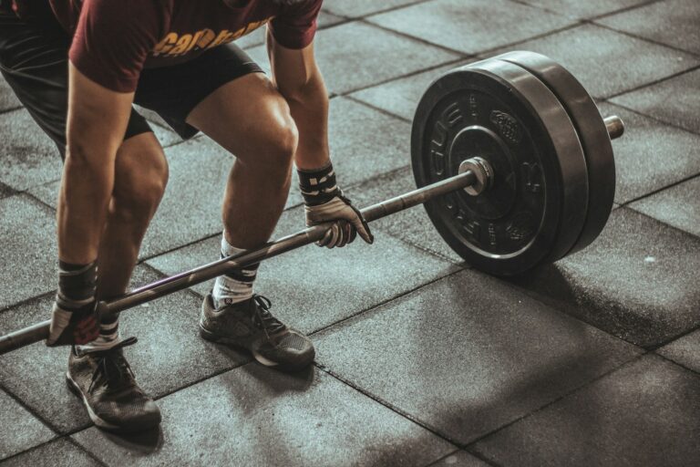 Trainingsplan Muskelaufbau: Sportler hebt eine schwere Langhantel vom Gummiboden im Fitnessstudio