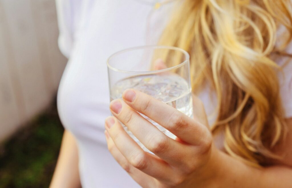 Frau hält ein Glas Wasser, denn Trinken hilft, wenn niedriger Blutdruck belastet