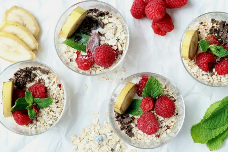 Vier Gläser Overnight Oats mit frischen Himbeeren und Bananenscheiben