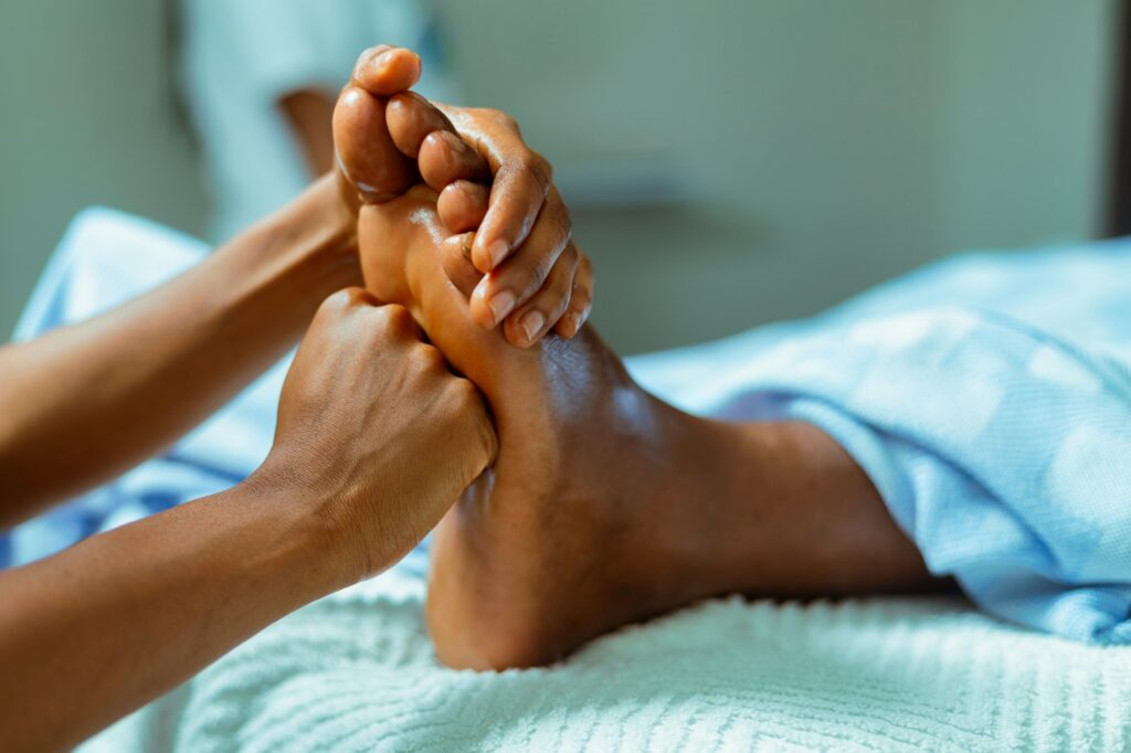 Hände massieren eine Fußsohle als Ergänzung zu Plantarfasziitis Übungen