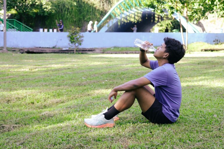 Mann sitzt nach dem Sport im Gras und trinkt Wasser aus einer Flasche