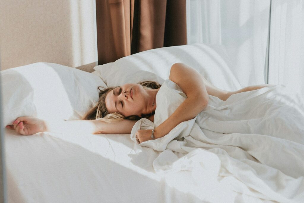 Person liegt entspannt im Bett, um am Abend früher Schlaf nachholen zu können