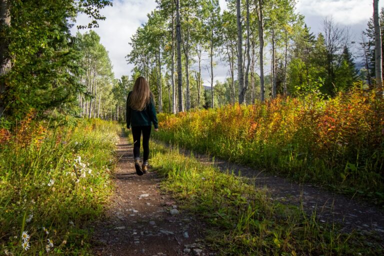 Frau spaziert tagsüber auf einem Weg zwischen Wiesen und Bäumen