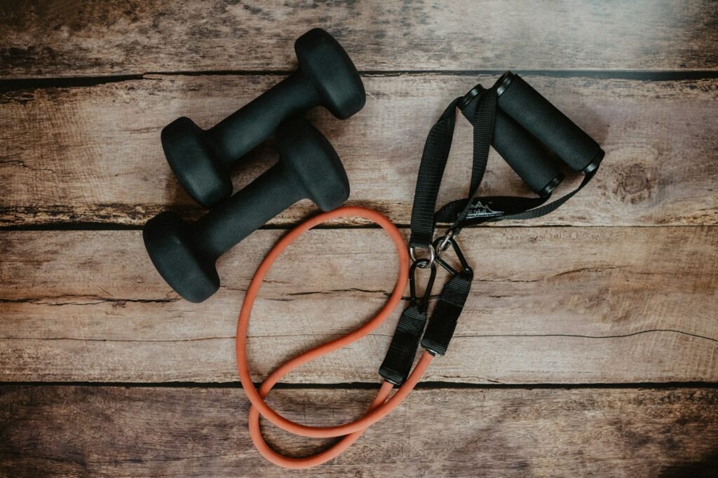 Orangefarbenes Fitnessband und Kurzhanteln auf Holz für Theraband Übungen zuhause