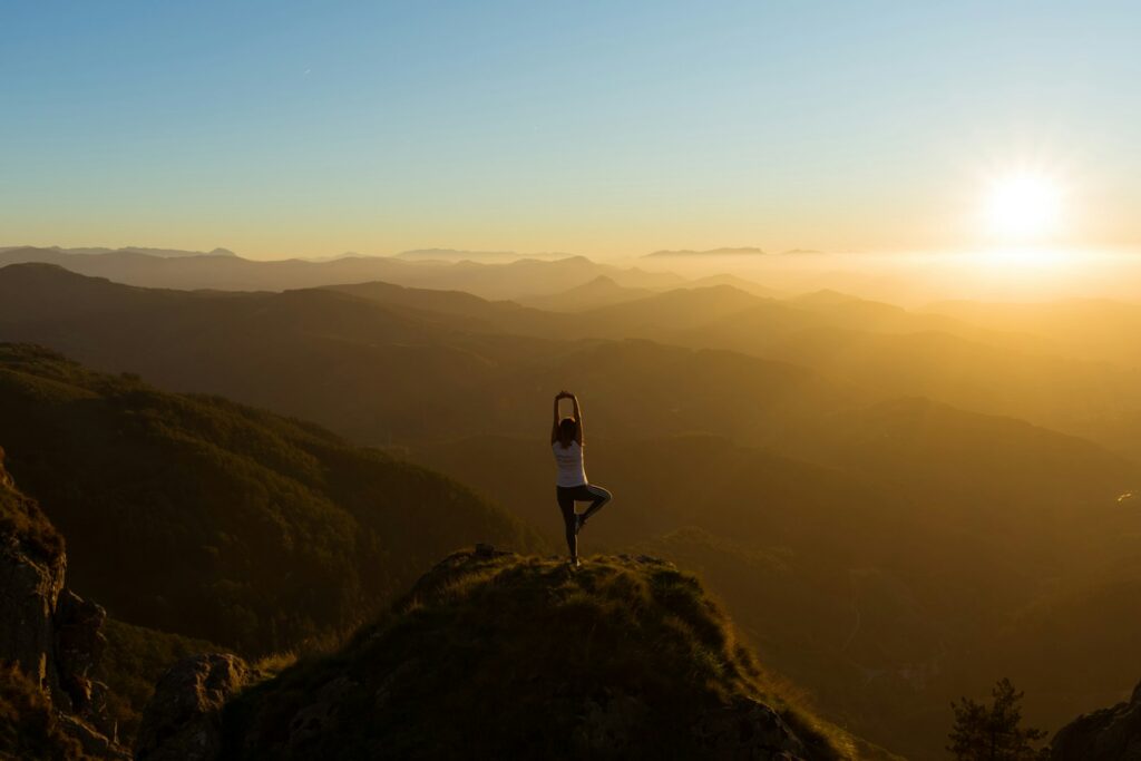 Frau dehnt sich bei Sonnenaufgang auf einem Berggipfel im Morgenlicht